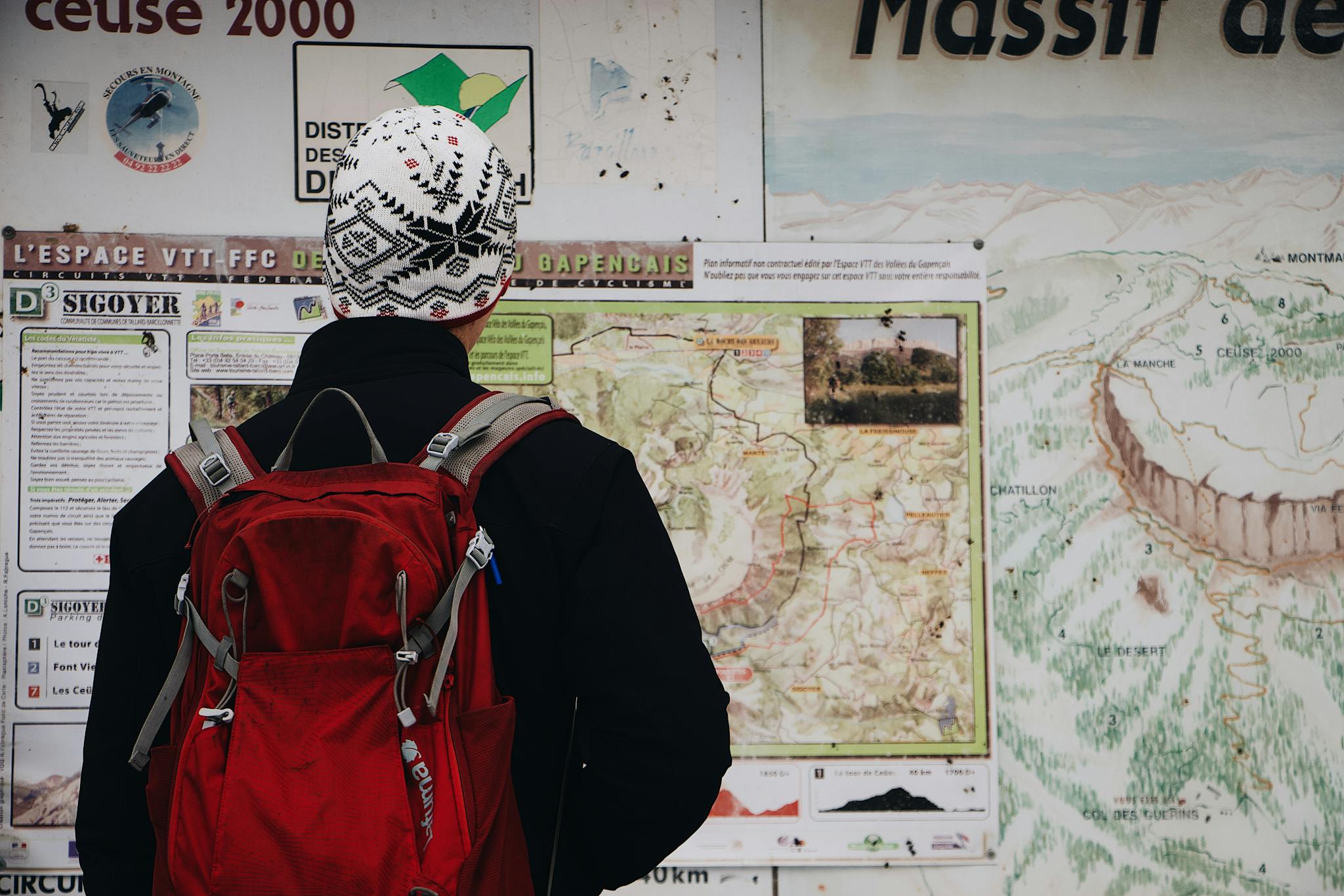 Person with a red backpack studying a detailed trail map in an outdoor mountain setting.